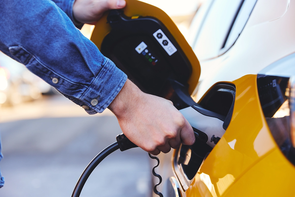 man charging a yellow electric car by the side of the road