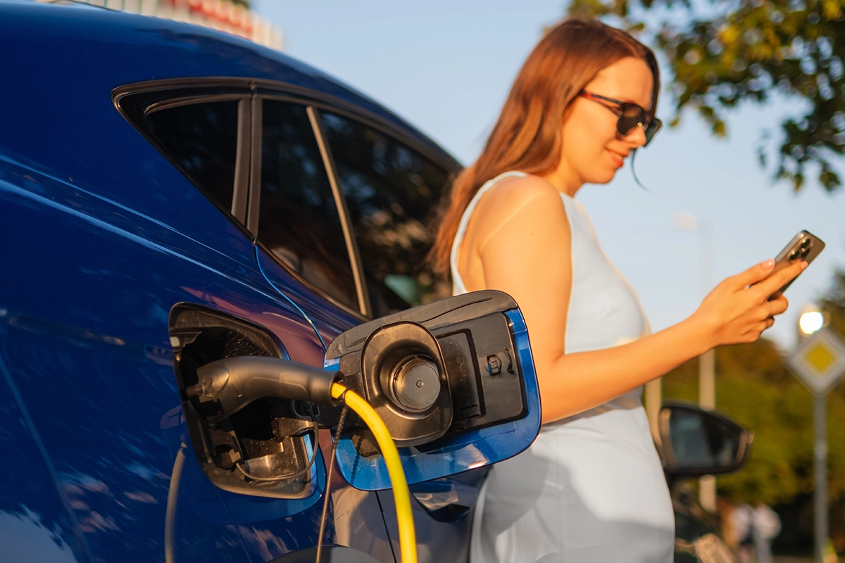 an electric vehicle charging in public as a woman with smartphone waits